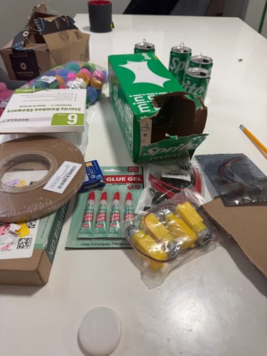 An image of various items on a table, including craft supplies and soda cans.