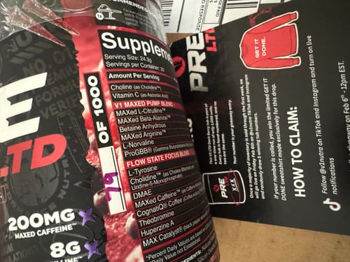 Customer's close-up of the V1 PRE WORKOUT tub, showing the supplement facts panel and a promotional card.