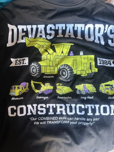 A close-up of the 'Devastator's Construction' graphic on the reviewer's black Transformers t-shirt.