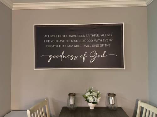 Customer's 'Goodness Of God Faith Sign II' displayed on a gray wall above a dark dining table.