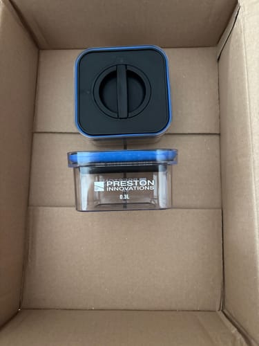 Recensent toont twee transparante 0,3L Preston Bait Safe-aasbakken in een doos, met zicht op de zijkant en deksel.