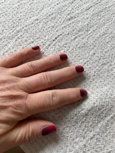 Hand einer Kundin, die die 'Taunted' UV-Gel-Nagelfolien auf kurzen Nägeln trägt und einen dunklen Bordeaux-Farbverlauf zeigt.