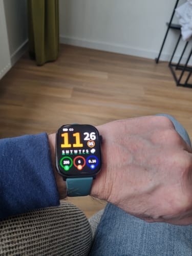Reviewer's wrist with a smartwatch personalized with a teal band and a colorful face.