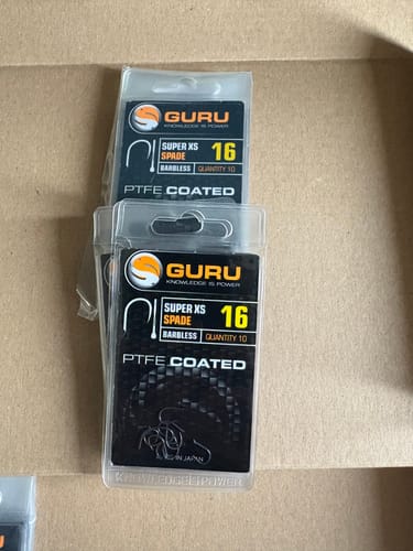 Klant toont twee verpakkingen Guru Super XS Spade weerhaakloze haken in maat 16.