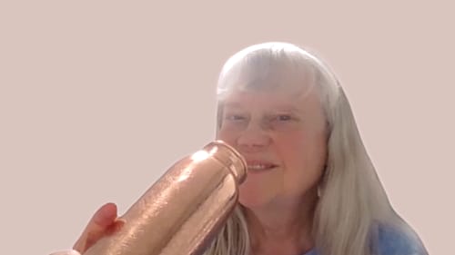 Close-up of a reviewer holding the shiny Mandala Engraved Copper Water Bottle near her face.