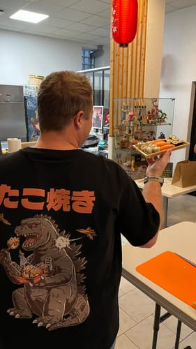 Customer seen from the back wearing the black Snackzilla T-Shirt, showing the large graphic while holding a plate of sushi.