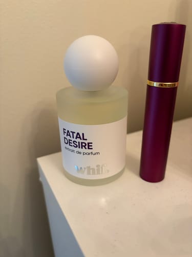 Customer's bottle of Fatal Desire perfume next to a purple travel atomizer on a white counter.