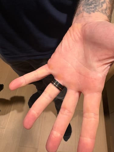 Customer's open hand showing The Loki ring, a black band with an offset rose gold inlay, on their ring finger.
