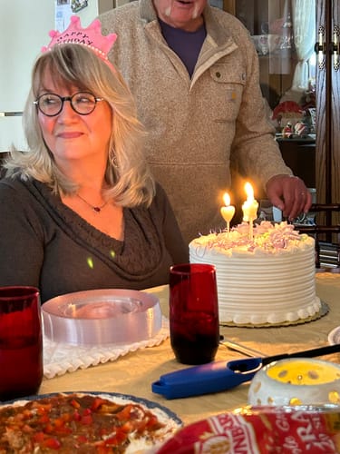 Customer celebrating her birthday, smiling at a table with a cake and lit candles.