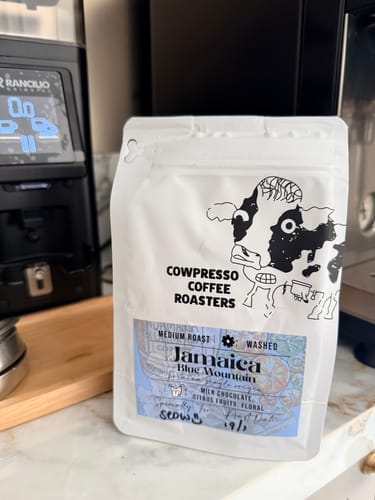 Reviewer's white pouch of Jamaica Blue Mountain Coffee on a counter next to a coffee grinder.