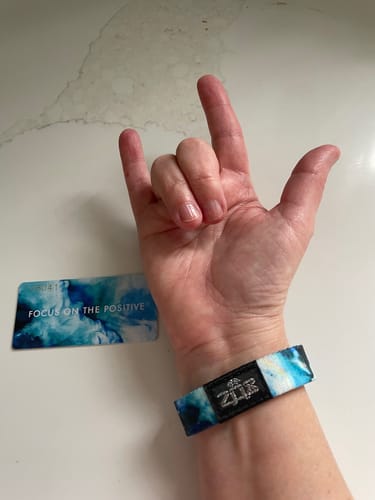 Customer wearing the blue and white Focus on the Positive bracelet while making an 'I love you' hand sign.