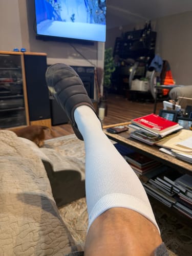 Reviewer relaxing with their leg propped up, wearing a white Performance Eucalyptus Compression Sock.