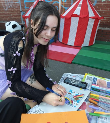 Reviewer sitting outside, wearing the black Alanis fishnet shrug with lilac bows while coloring.