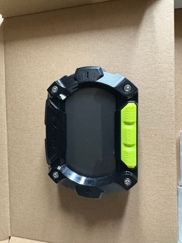 Recensent toont de zwarte Digital Clicker Pro met felgroene knoppen, liggend in de verpakking.