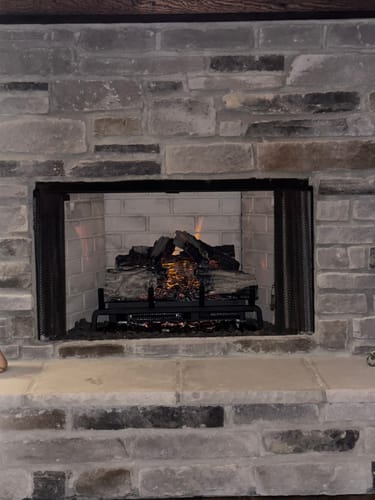 Customer's Napoleon Woodland 24'' Electric Log Insert installed in a stone fireplace, showing glowing logs and realistic flame effect.