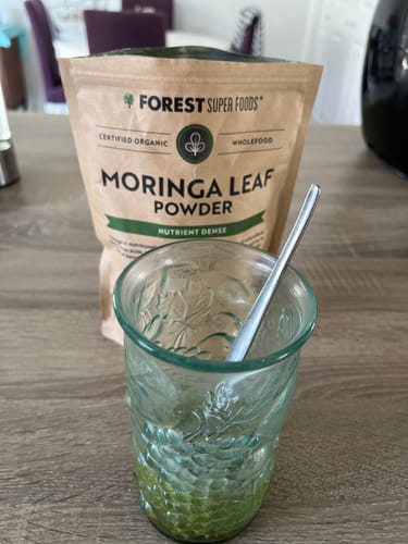 Customer's pouch of Organic Moringa Leaf Powder next to a prepared green drink in a glass.
