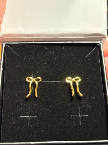 Customer's yellow gold Lola bow drop earrings shown inside their black jewelry box.