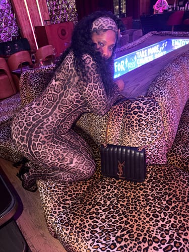 Customer wearing the Naked Print Closed Toe Jumpsuit and matching headband, posing on a patterned sofa.