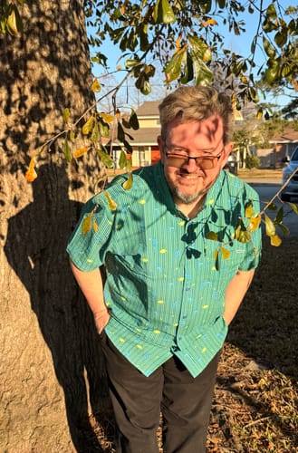 Reviewer smiling outdoors wearing the green, striped A Bug's Life 'It's an Ant Thing' seersucker shirt.