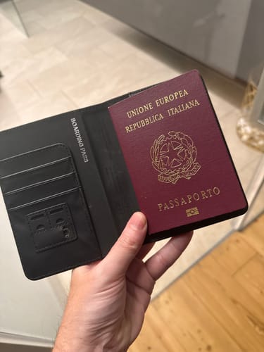 A reviewer holds the open black Trackable Passport Cover, showing an Italian passport inside and slots for cards.
