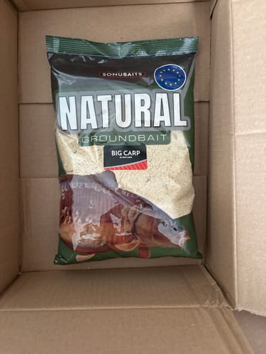 Klant toont de zak Sonubaits Natural Big Carp lokvoer in een kartonnen doos.