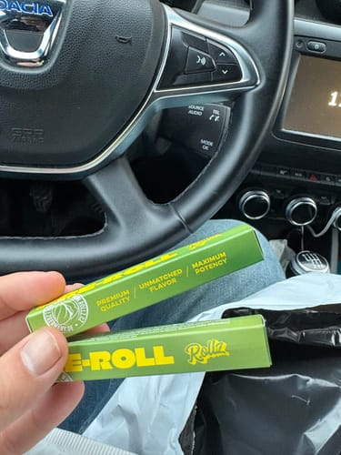 Customer holds two bright green boxes of ROLLZ THCA Pre-Rolls in their car.