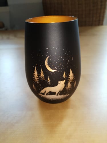 Kunde zeigt das schwarze Windlicht Nachtwolf mit goldenem Innenleben, das auf einem Holztisch steht.