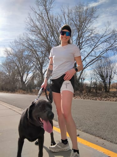 Customer standing on a sidewalk wearing the 'Child of God' Women's Performance Shorts with a dog.