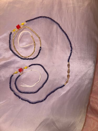 Customer displays their Azur Premium Tie On Waist Beads on a lavender surface. The beads are blue with red and yellow details.