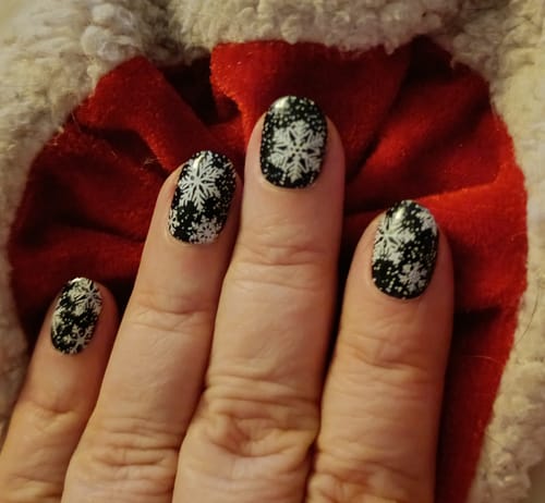 Nahaufnahme der Hand einer Kundin, die die festlichen 'Midnight Snow' UV-Gel-Folien mit Schneeflocken zeigt.