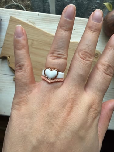 A customer's hand wearing the white silicone Heart Frame ring with a gold metal heart.