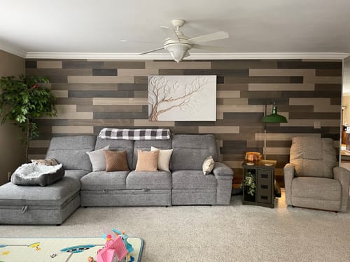 Customer's neutral branch canvas art mounted on a dark, planked wall above a large grey sofa.