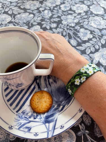 Reviewer's wrist wearing the green Special Memories Bracelet with a white floral pattern, next to a teacup and saucer.