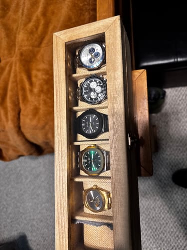 Reviewer's collection of watches in a wooden case, including the black and green Lucky Fours Brone models.