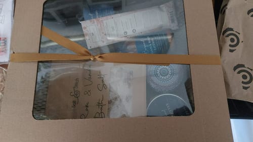 Customer's Opulent Oasis Gift Hamper in a gift box with a clear window, tied with a gold ribbon.