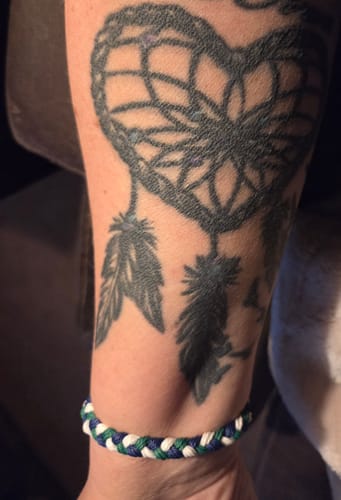 Reviewer wearing the blue, green, and white woven DAVID Bracelet on their wrist below a tattoo.