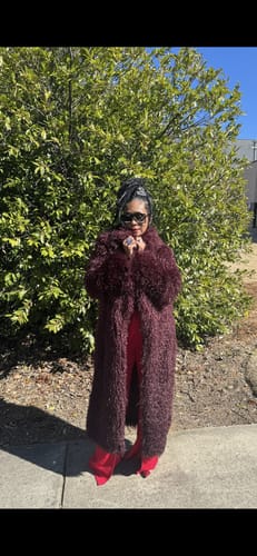 Reviewer wearing the lavish, dark Faux Fur Plush Long Coat over a red outfit outdoors.