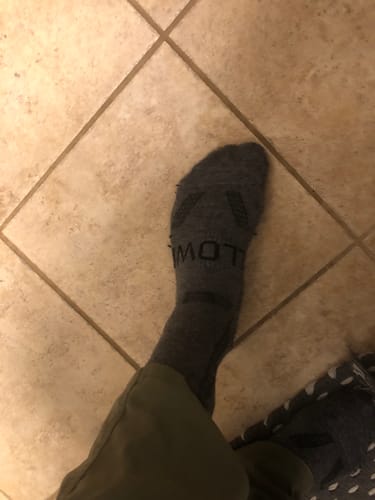 Customer's foot in a well-worn gray Men's Alpaca Sock on a tile floor, showing durability after a month of use.