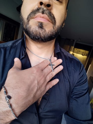 Un cliente con la mano en el pecho mostrando el colgante Crucifix sobre una camisa oscura.