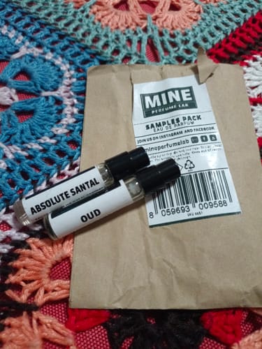 Cliente mostra i due campioni omaggio, "Absolute Santal" e "Oud", appoggiati sulla loro confezione.