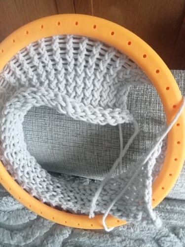 Customer using an orange circular knitting loom from the set to knit a grey blanket.