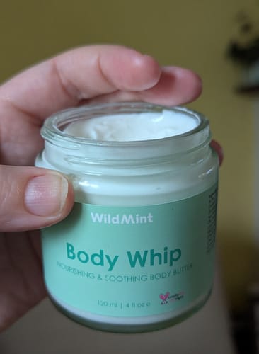 Customer holding an open jar of the Body Whip, showing its smooth, whipped texture.
