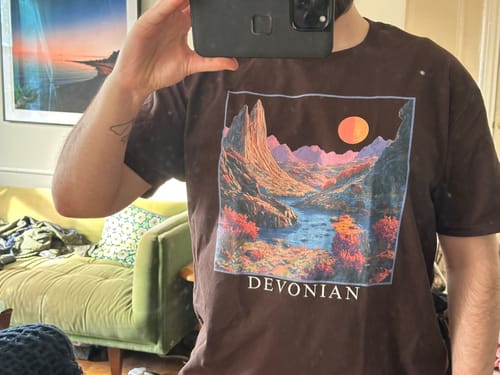 Customer wearing the brown Devonian Environment Graphic T-Shirt, showing the colorful landscape graphic.