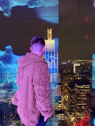 Reviewer from behind wearing the Geometric Jacquard Teddy Hoodie, looking out at a city skyline.