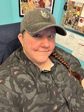 Reviewer smiling while wearing the dark gray 'Toothless' Dad Hat, showing its fit and embroidered design.