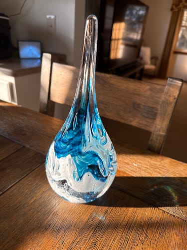 Reviewer's beautiful teardrop-shaped Dichroic Splash Flame on a wooden table, showing blue and white swirls inside the glass.