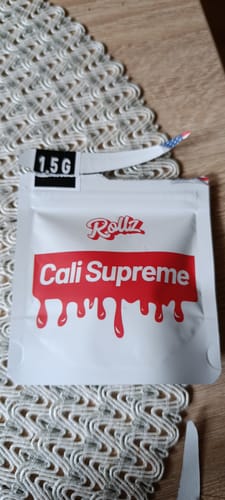 Customer's white 1.5G pouch of CALI SUPREME THCA Flower on a wooden table.