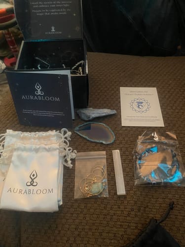 Customer's unboxed AuraBloom Subscription Box showing various crystals, jewelry, and branded pouches on a surface.
