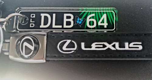 Close-up of a customer's custom QLD licence plate keychain with 'DLB 64' and a decorative palm frond design.