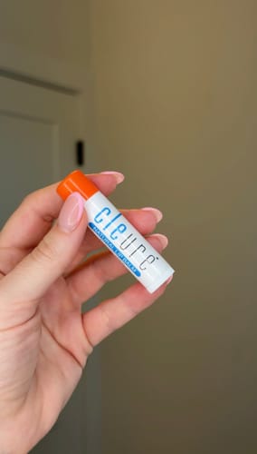 Customer holding the Lip Balm with Shea Butter, showing the white tube and bright orange cap.